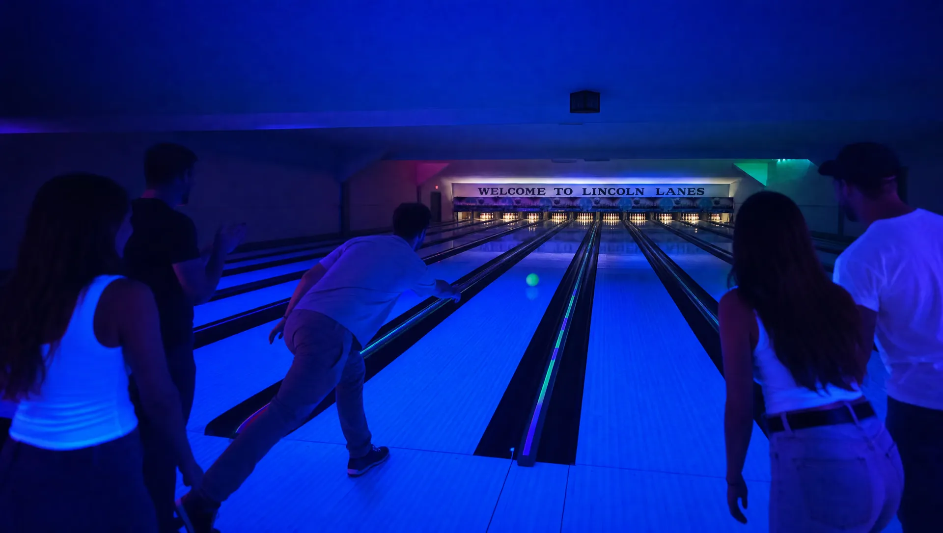 Friends celebrating under blacklight on the neon-lit lanes during glow bowling at Lincoln Lanes