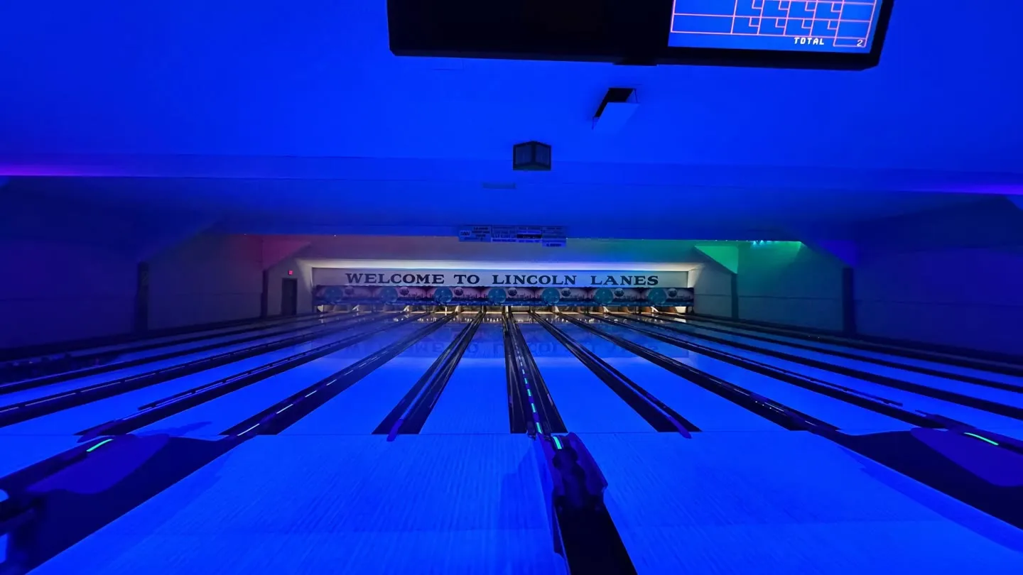 Looking down the glowing blue cosmic lanes toward the Welcome to Lincoln Lanes sign during glow bowling in Vernon, BC